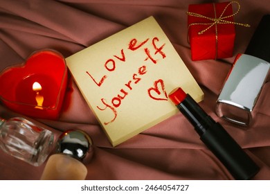 A note to self with call to love yourself drawing with red lipstick on a silk cloth flatly. A burning heart-shaped red candle, gift box Valentines Day - Powered by Shutterstock