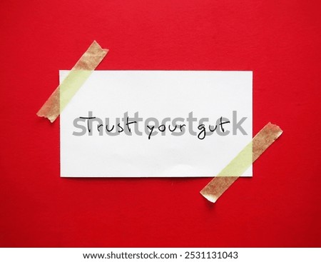 Note stick on red background with handwritten text TRUST YOUR GUT refers to trusting feelings of intuition. Following  instinct, can be valuable tool in some circumstances