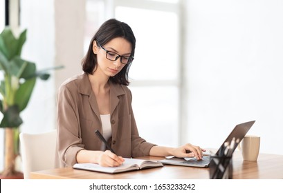 Note Taking. Portrait of female student using laptop and writing memo in her diary at modern office, copyspace - Powered by Shutterstock