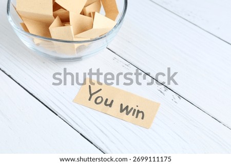 Note with text You Win and paper pieces on white wooden table, closeup