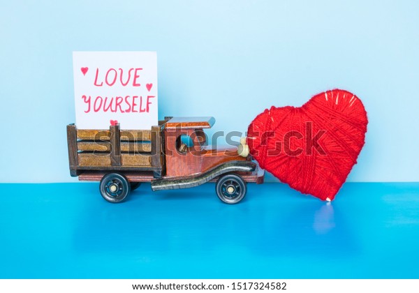 Note with words Love yourself, red heart and\
toy car on the blue background.\
