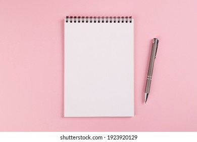 A notebook with a blank page and a ballpoint pen lie on a pink background. Copy space, layout, mockup. - Shutterstock ID 1923920129