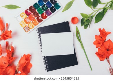 A notebook with a blank page sits on a table with a set of watercolors and a brush - Powered by Shutterstock