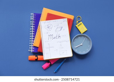 Notebook with calculator, alarm clock and school stationery on blue background