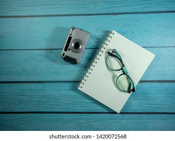 Notebook, camera and glasses placed on a blue wooden table Travel equipment