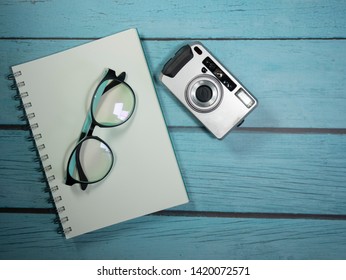Notebook, camera and glasses placed on a blue wooden table Travel equipment