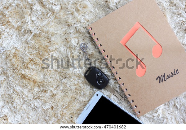 Notebook with car key and mobile phone on brown shaggy\
carpet 