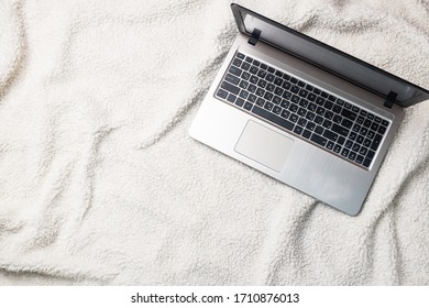 Notebook Computer lying on a white wool blanket. Concept of working and learning at home. Copy space.