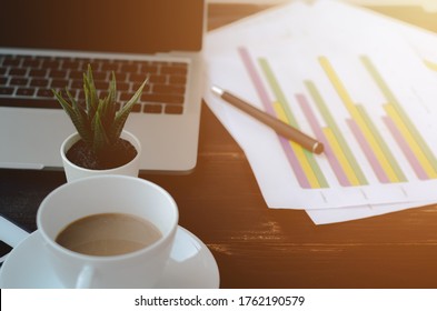 A notebook computer on the table.Brown table top There is equipment to work on it.A white coffee cup placed on the table.Do not focus on the object.