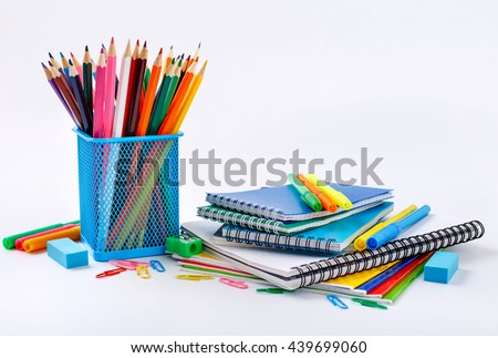 Notebook and copybook stack with metal holder pencils, pens, paper clips, sharpener and eraser on a white background. Back to school concept