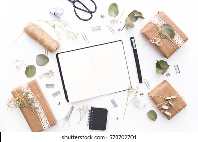 Notebook With Craft Boxes And Green Branches On White Background. Wedding Planning. Flat Lay, Top View