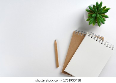 Notebook With Craft Paper, Pencil, Green Plant On White Background. Workspace Concept. Top View, Copy Space, Mockup, Flat Lay 