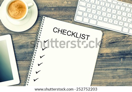 Notebook, digital tablet pc, keyboard and coffee on wooden background. Mock up in Instagram style with sample text Checklist