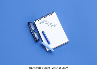 Notebook with empty to do list, markers and eyeglasses on blue background. New year goals