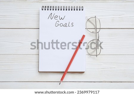 Notebook with empty to do list, pencil and eyeglasses on white wooden background. New year goals