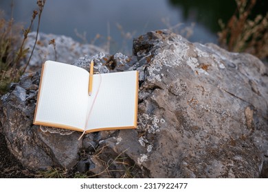 the notebook is empty, open on a stone in the forest, the background is blurred by nature. writing a book in nature, inspiration on the mountain