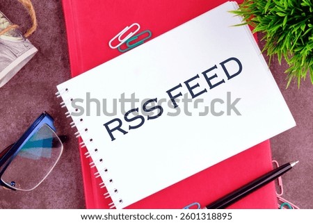 A notebook featuring the term RSS feed rests on a textured surface alongside office supplies, illustrating subscription management in digital content environments.