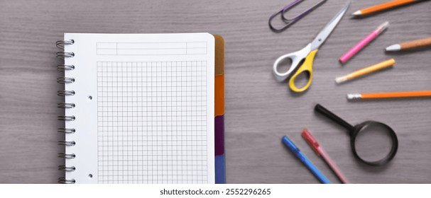 Notebook with graph paper and various colorful school supplies arranged on a gray wooden table, creating a learning or studying concept. Back to school banner - Powered by Shutterstock