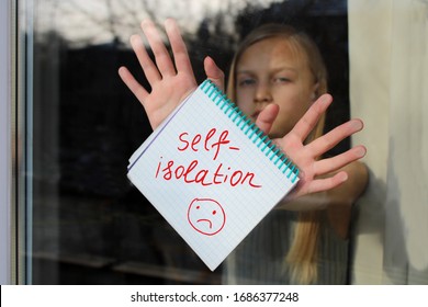 A notebook with the inscription Self Isolation in the hands of a girl behind the glass of the apartment. Quarantine or self-isolation due to the pandemic of Covid-19. Self-isolation sign. Stay at home