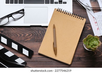 Notebook with laptop, eyeglasses and movie clapper on dark wooden background