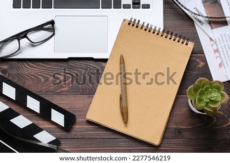 Notebook with laptop, eyeglasses and movie clapper on dark wooden background