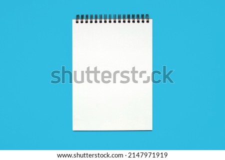 Notebook made of white paper with binding on a blue background. Blank notepad with free space for text. Notebook in classic binding without notes, top view