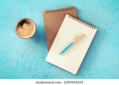Notebook mockup with a pen and a cup of coffee, overhead flat lay shot on a blue background