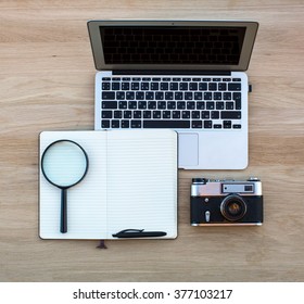 Notebook, notepad with pen, magnifier and camera is laid out on a wooden surface.
