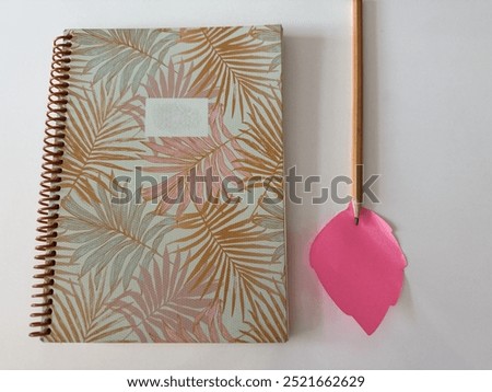 Notebook, notepaper and pencil. Notebook with leaf pattern, pink leaf-shaped notepaper and yellow pencil lie on white table. Notepaper and notebook with copy space. Copy space for text. Close-up.