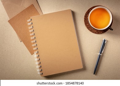 A notebook on a desk, shot from the top on a rustic background with a cup of tea and a pen