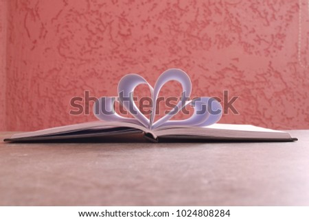 Notebook on light brown grey table on pink background. Heart shapes from sheets of book on pink background. Opened blank decorative notebook. Concept of inspiration and writing.