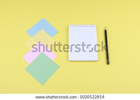 Notebook on office table with a cup of coffee, plant, stationery and office supplies. Blank notepad paper for input copy or text. Top view desk, flat lay yellow color background concept.