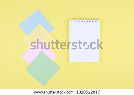 Notebook on office table with a cup of coffee, plant, stationery and office supplies. Blank notepad paper for input copy or text. Top view desk, flat lay yellow color background concept.
