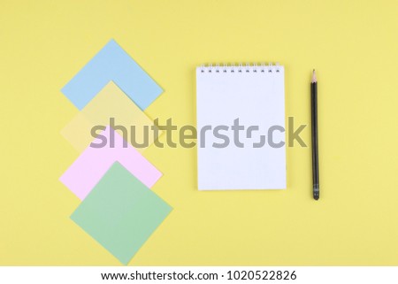 Notebook on office table with a cup of coffee, plant, stationery and office supplies. Blank notepad paper for input copy or text. Top view desk, flat lay yellow color background concept.