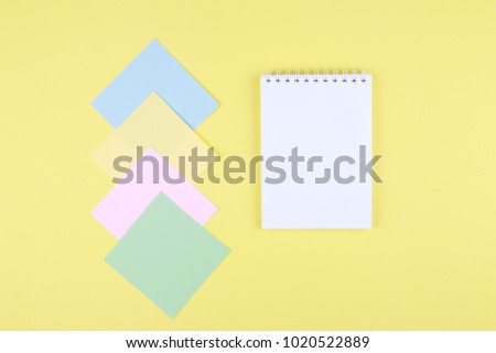 Notebook on office table with a cup of coffee, plant, stationery and office supplies. Blank notepad paper for input copy or text. Top view desk, flat lay yellow color background concept.
