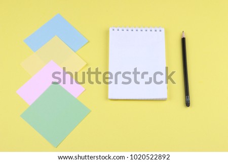 Notebook on office table with a cup of coffee, plant, stationery and office supplies. Blank notepad paper for input copy or text. Top view desk, flat lay yellow color background concept.