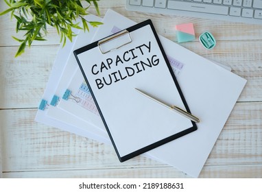 A notebook on a spring with the text CAPACITY BUILDING on a white sheet lies on a wooden table with colored pens. Business concept. - Shutterstock ID 2189188631