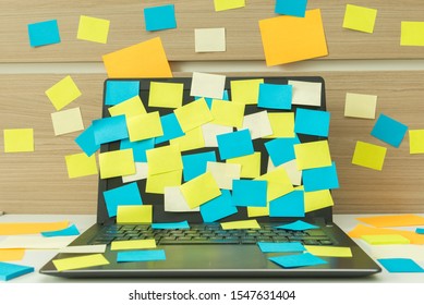 Notebook on white table with some sticky notes stuck on the wall. Sticky Note Papers on Notebook computer Screen. Concept of many tasks, hard work, overloaded, overtime and deadline.