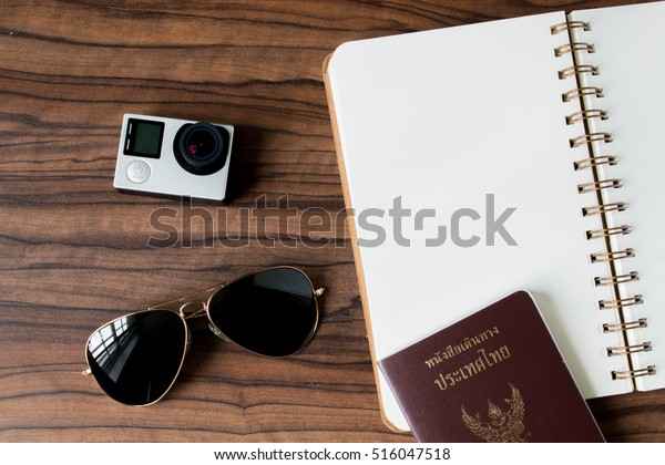 Notebook, passport sunglasses and action camera on\
top table view angle