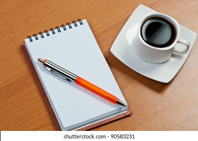 Notebook with pen and coffee on table.