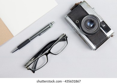 notebook with pen , glasses and camera on desk with white fabric background