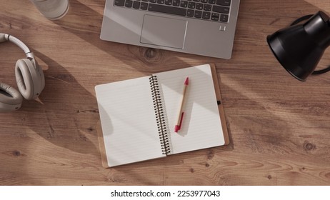 notebook with pen made of recyclable materials, cardboard, lies on desktop in office or home office next to laptop, headphones and table lamp. Preparation for online study, top down view. - Powered by Shutterstock