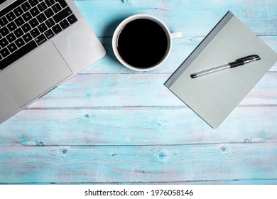 Notebook and pen next to open laptop computer and cup of black coffee for home office working or student studying on a weathered blue wood background with copy space and room for text - Powered by Shutterstock