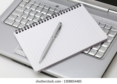 A notebook and pen resting on a laptop PC