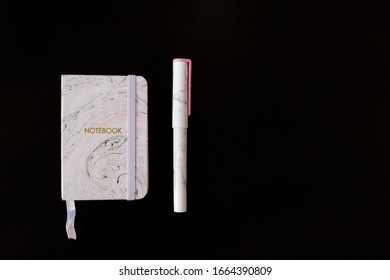 Notebook and pen with trendy marble pattern lie on black background top view. Picture with copy space