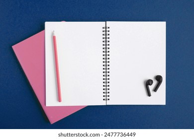 Notebook and pencil, wireless headphones. Open notebook on dark blue color background, spiral notepad. Top view. Notepad with blank white pages for write, office flat lay. Copy Space. Navy. To do list - Powered by Shutterstock