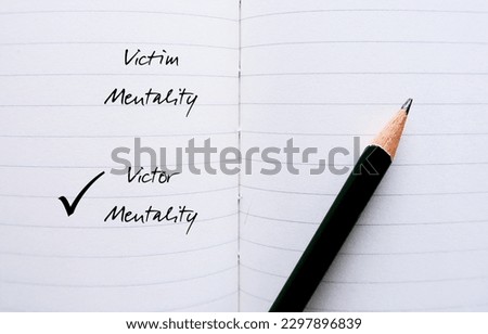 Notebook with pencil writing VICTIM and VICTOR MENTALITY, to overcome feeling like have no control over things  and start developing growth mindset or positive attitude to improve position