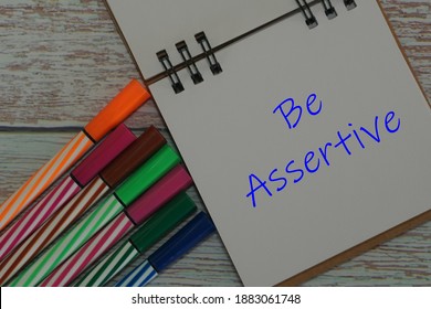 a notebook and pens color with word Be Assertive