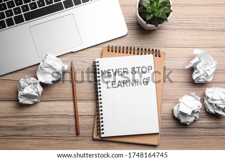 Notebook with phrase NEVER STOP LEARNING and crumpled paper on wooden table, flat lay