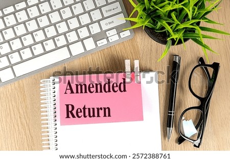  Notebook with a pink note labeled Amended Return clipped on top, placed on a wooden desk with a keyboard 